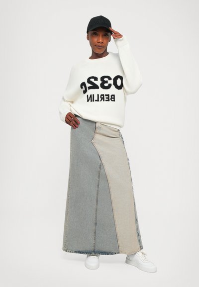Denim maxi skirt with color-blocked panels in light and dark gray, paired with a white knit sweater featuring bold black text and white sneakers.