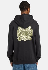 Hoodie noir avec un grand motif graphique vert au dos, mettant en avant une texture bois et des éléments de skateboard. Matière en mélange de coton.