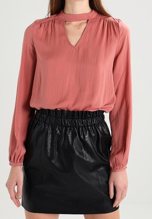 Blusa a maniche lunghe color ruggine con scollatura a V e spalle arricciate, abbinata a una minigonna nera in finta pelle con cintura elastica.