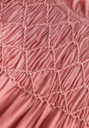 Rózsaszín anyag, majdnem bőrszínű, gyűrt textúrával, gyémánt alakú ráncolással, amely fonott szálakból készült és sima, könnyű anyagú.