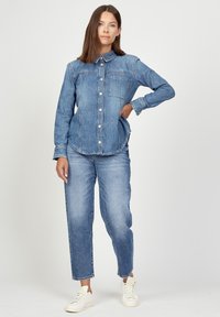 Denim button-up shirt with a collar, chest pocket, and long sleeves. Paired with light-wash straight-leg jeans and white sneakers.
