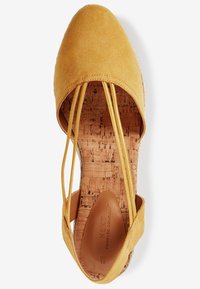 Espadrille en suède jaune avec des sangles élastiques ; semelle en liège avec un logo en relief ; design à bout rond ; semelle extérieure plate et texturée.