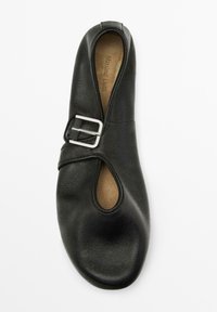 Schwarzer Lederschuh mit offenem Zeh, geschwungenem Ausschnitt und seitlichen Schnallendetails. Weicher Stoff und flache Sohle. Innenfarbe ist hellbraun.