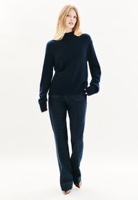 Maglione a maglia blu notte con collo alto, abbinato a jeans flared in denim scuro. Maniche con polsini a coste ben visibili e design aderente. Gli stivali hanno una finitura metallica.