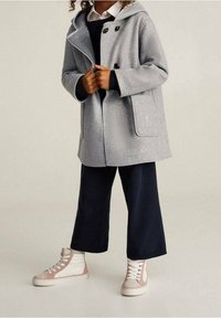 Manteau en laine gris avec une capuche, deux poches avant et des boutons noirs. Associé à un pantalon large bleu marine et des baskets blanches avec des accents roses.
