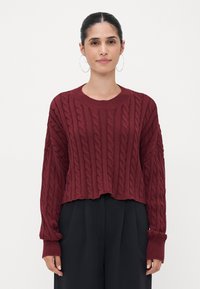Burgundy cable-knit sweater with a cropped design, wide sleeves, and ribbed cuffs, paired with black, loose-fitting trousers.