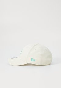 Hvit bomullslue med en buet skjerm, med lys grønn brodert logo og sømmer. Sidepanelet viser en liten logodetalj.
