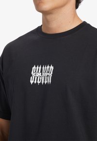 Black cotton t-shirt featuring a central white graphic logo. The design includes distorted lettering with a textured appearance.