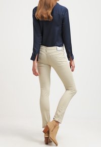 Mörkblå långärmad blus i kombination med åtsittande beige byxor och bruna ankelboots. Blusen har en mjuk textur och en subtil lyster.