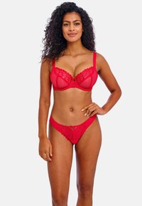 Bralete de encaje rojo con copas transparentes y bordes festoneados, combinado con unas braguitas de bikini de encaje rojo a juego que presentan un pequeño lazo como detalle.