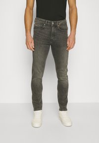 Šedé slim-fit džíny z denimu s vybledlým umytím, pěti kapsami a kontrastním oranžovým šitím, spárované s bílými teniskami.