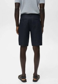 Pantaloni corti blu navy con una linea dritta, realizzati in tessuto leggero. Due tasche posteriori con dettagli sottili. Abbinati a sandali neri.