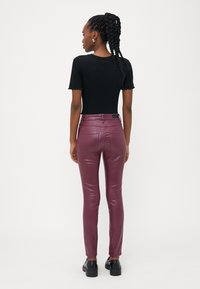 Top preto de malha com mangas cortas, combinado com calças justas brilhantes em bordô e sapatos pretos, com uma textura suave e bolsos traseiros funcionais.