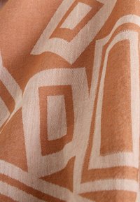 Tissu marron clair avec des motifs géométriques rectangulaires blancs, montrant la texture et de légers plis.