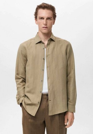 Lys beige skjorte med knapper og lodrette hvide striber, med krave, lange ærmer og glat tekstur. Bæres over en hvid top.