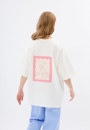 Witte oversized t-shirt met een roze grafiek op de achterkant, met lijntekening van een koffiepot, kopje en croissant. Zacht katoenmateriaal.