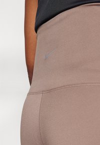 Nike tajice od meke taupe tkanine s glatkom teksturom. Imaju suptilni sivi logo i šavove za prilagođen izgled.