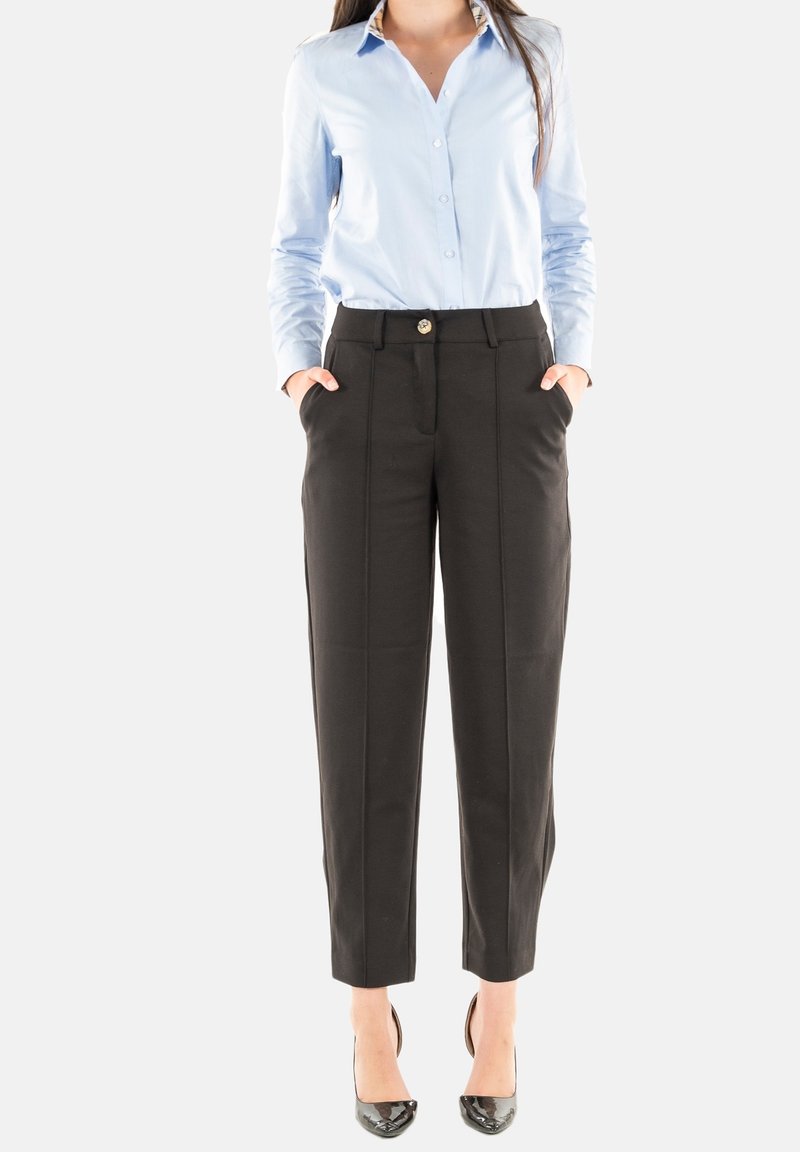 Camicia button-up azzurro chiaro, pantaloni neri su misura con tasche frontali e bottone dorato. Tacchi neri lucidi. Tessuto morbido, vestibilità su misura.