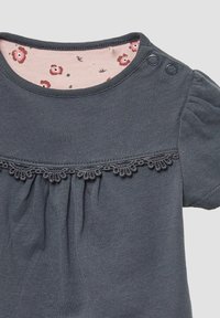 Donkergrijze babysweater met kantafwerking onder de borst, korte pofmouwen, twee drukknoopjes op de schouders en een roze bloemenvoering in de halslijn.