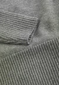 Pehmeä harmaa neulottu kangas, jossa näkyy neulotut resorit hihansuut ja vyötärönauha villapaidassa.