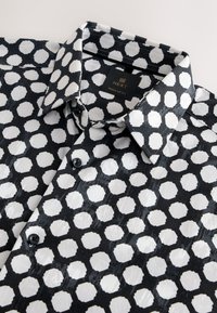 Camicia bianca e nera con motivo esagonale, tessuto liscio, chiusura con bottoni e colletto con etichetta che indica "NEXT, Regular Fit."
