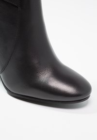 Bottine en cuir noir à bout pointu, texture lisse, quincaillerie minimale, silhouette élégante. Détail subtil de couture sur le côté.