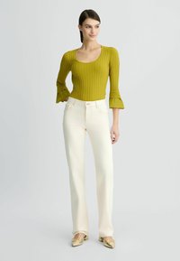 Haut côtelé vert olive avec des manches évasées, associé à un pantalon crème ajusté et des ballerines dorées avec un accent nœud. Design simple et épuré.