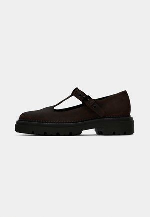 Brown leather Mary Jane shoes with a cutout design, featuring a strap with a buckle, a thick black rubber sole, and contrasting stitching detail.