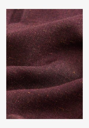 Burgundy textured fabric with a woven pattern, showing variations in color, featuring small flecks of orange and yellow throughout.