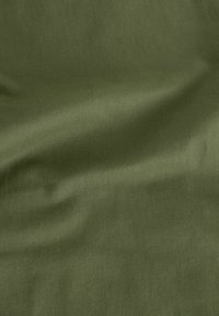 Oudgroene stof met een gladde textuur en een diagonaal geweven patroon, waarbij subtiele licht- en schaduwvariaties zichtbaar zijn.