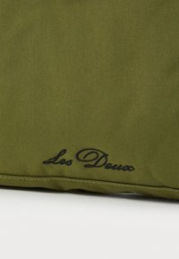 Olijfgroene stoffen tas met een gladde textuur, voorzien van een geborduurd zwart logo "Les Deux" aan één kant. Eenvoudige rechthoekige vorm.