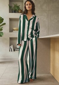 Ensemble de pyjama à rayures vertes et roses, comprenant une chemise à col avec une poche et un pantalon à jambes larges, fabriqué dans un matériau doux et léger.