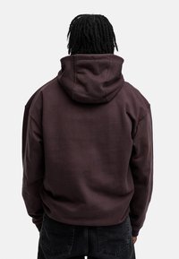 Dunkelbrauner Pullover-Hoodie aus weichem, strukturiertem Stoff. Verfügt über eine große Kapuze und eine entspannte Passform, mit gerippten Bündchen und Saum.