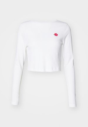 Top blanco de manga larga y recortado, hecho de un tejido suave, con un pequeño bordado de una rosa rosa en el lado izquierdo del pecho. Diseño simple, sin patrones.