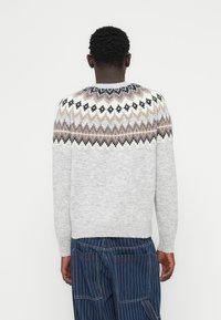 Γκρι  πλεκτό πουλόβερ με στρογγυλή λαιμόκοψη, με διακοσμητικό σχέδιο στον ώμο σε μπεζ, μαύρο και λευκό. Μαλακή υφή, μακριά μανίκια και ριμπ μανσέτες.