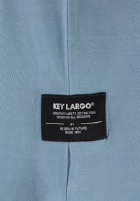 Blauwe textiel met een zwart merklabel met witte tekst. Het label bevat de merknaam "KEY LARGO" en ontwerpdetailles in een rechthoekige vorm.