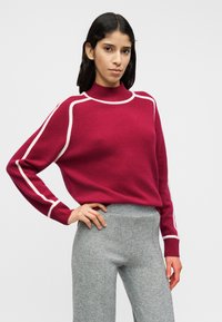 Pull en tricot fuchsia avec un col montant et des lignes d'accent blanches, associé à un pantalon en mélange de laine gris avec une coupe ajustée.