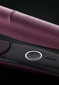 GHD Chronos haarstyler met een donkerpaarse metalen behuizing, glanzend zwarte accenten, een aan/uit-knop met een circulair ontwerp en een gestructureerd oppervlak.
