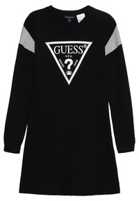 Černé dlouhé šaty s dlouhým rukávem, na kterých je trojúhelníková stříbrná nášivka s textem "GUESS U.S.A." a otazníkem uvnitř designu. Šedé akcenty na ramenech.