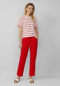 Biała i czerwona pasiasta bluzka z krótkim rękawem zestawiona z luźnymi czerwonymi spodniami i białymi sandałami. Materiał wydaje się miękki i przewiewny, z elastycznym pasem ze sznurkiem.