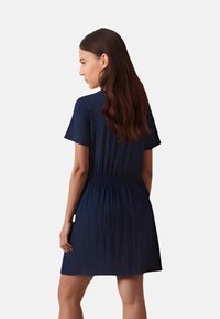 Abito blu navy a maniche corte con vita arricciata, realizzato in tessuto testurizzato, caratterizzato da una vestibilità rilassata e un design semplice e lineare.