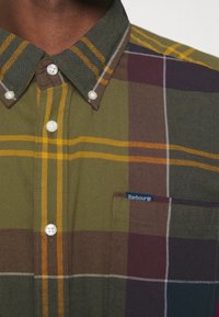 Zelená kostkovaná košile vyrobená z bavlny. Obsahuje perleťové knoflíky, kapsu s brandingem Barbour a střídající se horizontální a vertikální pruhy.