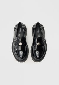 Czarne lakierowane buty ze skóry z zaokrąglonym noskiem, grubą podeszwą i ozdobnym metalowym akcentem z przodu. Proste przeszycia wzdłuż krawędzi.