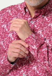 Overhemd met knoopsluiting in een roze en bordeaux bladpatroon, met een kraag en witte knopen. De stof lijkt glad met een lichte glans.