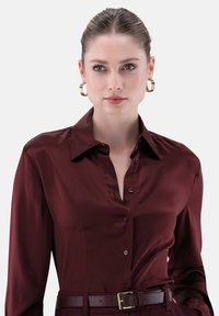 Maroon satin blouse with a collared neckline, button front, and long sleeves, paired with a matching belt featuring a gold buckle.