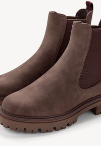 Stivali ankle in pelle marrone con pannelli laterali elasticizzati, superficie testurizzata e suole in gomma spesse. Cuciture dettagliate sulle giunture.