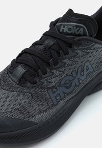 Chaussure de sport noire avec un dessus en tissu texturé, arborant le logo HOKA, des lacets plats et une semelle épaisse et rembourrée pour un soutien optimal.