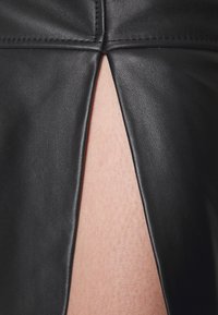 Svart läderplagg med en central slits som avslöjar ljus hud under, vilket visar detaljerad textur och sömnad av materialet.