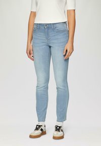 Jasnoniebieskie dżinsy skinny wykonane z denimu. Charakteryzują się średnim stanem, przednimi i tylnymi kieszeniami oraz subtelnym przetarciem. Połączone z czarno-białymi butami sportowymi.