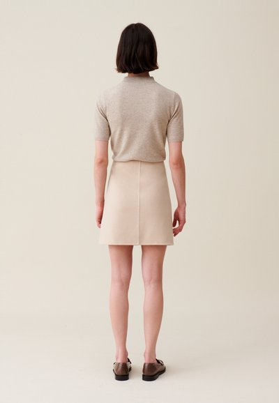 Camisa polo de manga corta beige con cuello combinada con una falda corta en línea A beige. Unos zapatos marrones completan el conjunto. Texturas suaves, diseño sencillo.